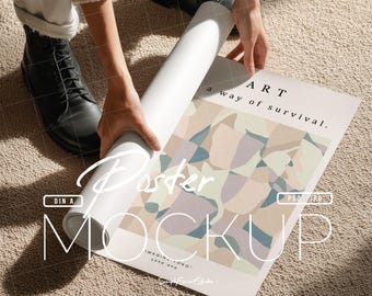 Op de afbeelding: Een opgerolde witte poster wordt uitgerold om een kleurrijk abstract ontwerp te onthullen met de woorden "ART a way of survival". De poster ligt op een beige tapijt.