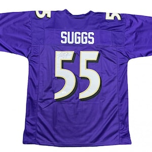 May include: A purple football jersey with the name "SUGGS" and the number "55" in white and gold. The jersey has a signature above the number. The sleeves have black trim.