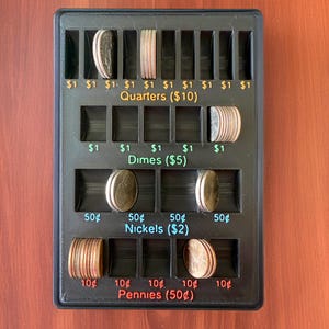 Pode incluir: Uma bandeja de moedas de plástico preto com compartimentos para classificar a moeda americana. A bandeja tem etiquetas para quartos, dimes, níqueis e centavos, com o valor total de cada tipo de moeda indicado entre parênteses. A bandeja está cheia de várias moedas americanas.