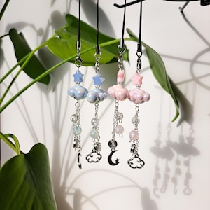 Peut inclure: Trois breloques de téléphone avec un design nuage et étoile. Les breloques sont faites de perles blanches et bleues, et les lanières sont noires. Les breloques sont suspendues à des chaînes argentées.