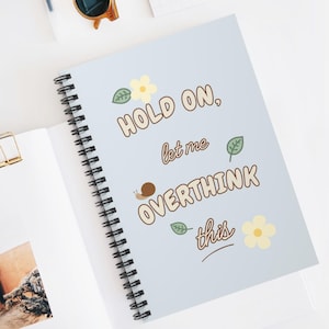 以下が含まれることがあります： 茶色の文字で「HOLD ON, let me OVERTHINK this」と書かれた青いスパイラルノート。ノートには、カタツムリ、葉、花が茶色、緑、黄色で描かれている。