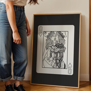 Puede incluir: Impresi&oacute;n art&iacute;stica enmarcada en blanco y negro que presenta una ilustraci&oacute;n estilizada de dos reinas bes&aacute;ndose, al estilo de una carta de juego. La obra de arte est&aacute; sobre un fondo negro con un marco dorado. La carta est&aacute; etiquetada con un coraz&oacute;n y una pica.