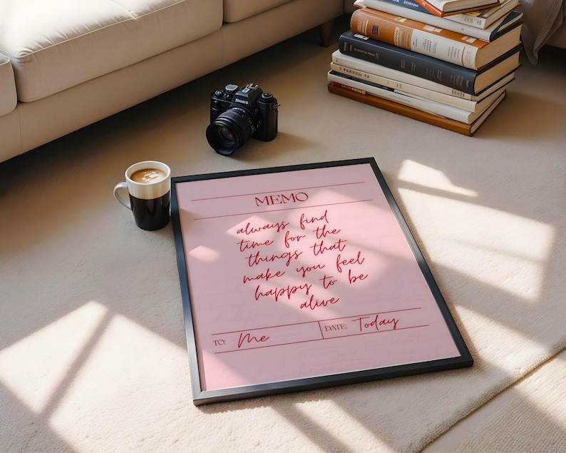 May include: A framed pink memo with the text "always find time for the things that make you feel happy to be alive." A black camera, a coffee mug, and a stack of books are also visible.