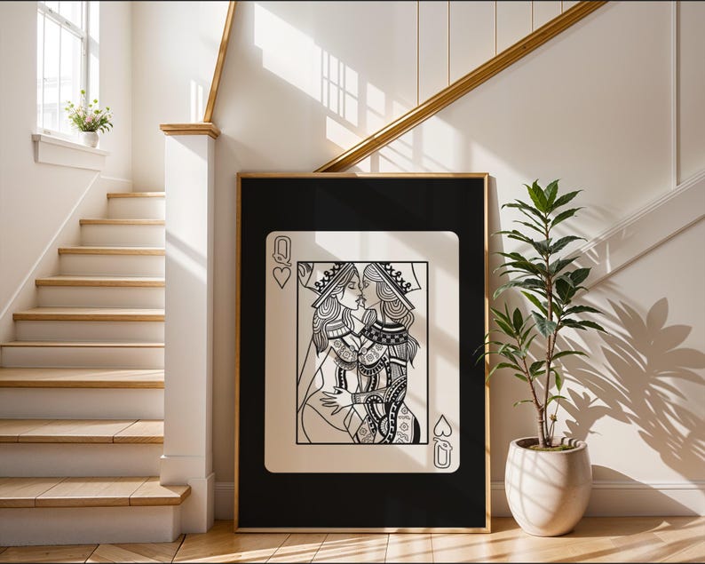 Puede incluir: Una impresi&oacute;n art&iacute;stica enmarcada que presenta una ilustraci&oacute;n en blanco y negro de dos reinas bes&aacute;ndose, sobre un fondo negro. La obra de arte est&aacute; dise&ntilde;ada como una carta de juego, con el s&iacute;mbolo de la Reina de Corazones visible. El marco es dorado y la impresi&oacute;n se exhibe en un interior moderno y luminoso.