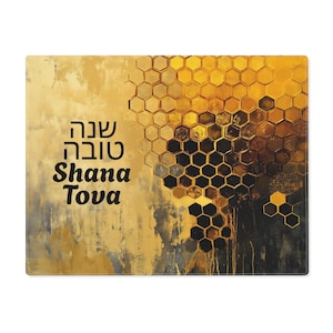 May include: Rectangular placemat with a textured abstract design in shades of gold, black, and grey. The right side features a honeycomb pattern. The text "Shana Tova" is printed in black. A decorative item for the home.