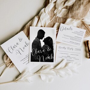 Könnte beinhalten: Hochzeits-Einladungssuite mit einer Schwarzweiß-Silhouette eines Paares auf der Vorderseite. Die Einladung enthält die Namen "Clara & Noah" und das Datum "Sonntag, 29. Oktober". Die RSVP-Karte enthält den Text "Bitte antworten" und ein Menü mit Optionen für Hähnchen, Fisch und vegetarisch.