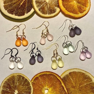 May include: A selection of teardrop earrings in shades of orange, pink, purple, white, and yellow. The earrings are presented alongside dried orange and lemon slices, highlighting the jewellery's colours and design.