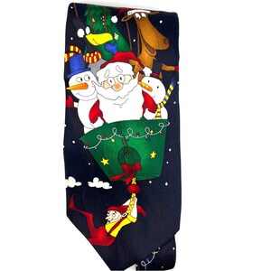 May include: A navy blue Christmas-themed tie featuring Santa Claus, snowmen, and a reindeer in a green basket. A cartoon elf is hanging from the basket. The tie has a festive design with a night sky background and white snowflakes.