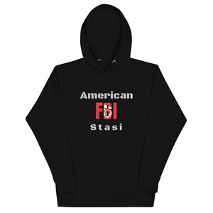 Può includere: Felpa con cappuccio nera con il testo "American FBI Stasi" in lettere bianche e rosse.