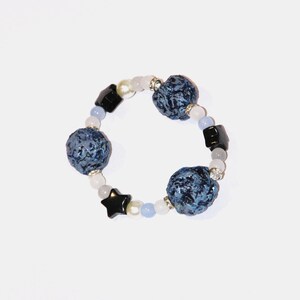 May include: A blue and black beaded bracelet with star-shaped charms. The bracelet is made with blue and white beads, and black star-shaped charms.
