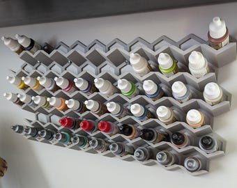 May include: A gray hexagonal shelf unit with multiple rows of small bottles of paint. The bottles are arranged in a staggered pattern and are of various colors, including red, blue, green, and yellow.