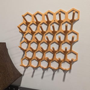 May include: A wall-mounted honeycomb-shaped storage rack with multiple hooks. The rack is made of a light brown plastic and has a modern design.
