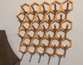 May include: A wall-mounted honeycomb-shaped storage rack with multiple hooks. The rack is made of a light brown plastic and has a modern design.