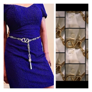May include: A gold chain belt with a large, double-V logo buckle. The belt is worn over a royal blue dress.