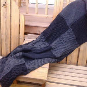 May include: A large, gray and black knitted throw blanket with a cable knit pattern. The blanket is draped over two wooden chairs.