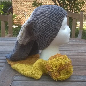 Puede incluir: Un gorro de punto gris y amarillo con una corona larga y puntiaguda y un gran pomp&oacute;n amarillo.