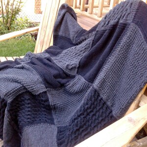 May include: A gray and black knitted throw blanket with a cable knit pattern. The blanket is draped over a wooden chair.