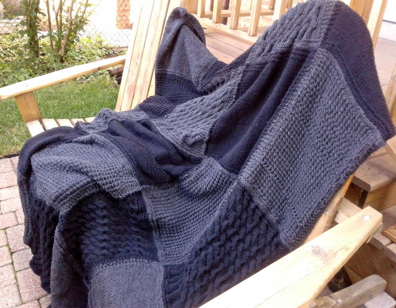 May include: A gray and black knitted throw blanket with a cable knit pattern. The blanket is draped over a wooden chair.