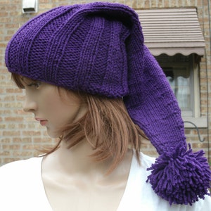 May include: Purple knitted hat with a long, pointed top and a fluffy pom-pom. The hat is made with a cable knit pattern.