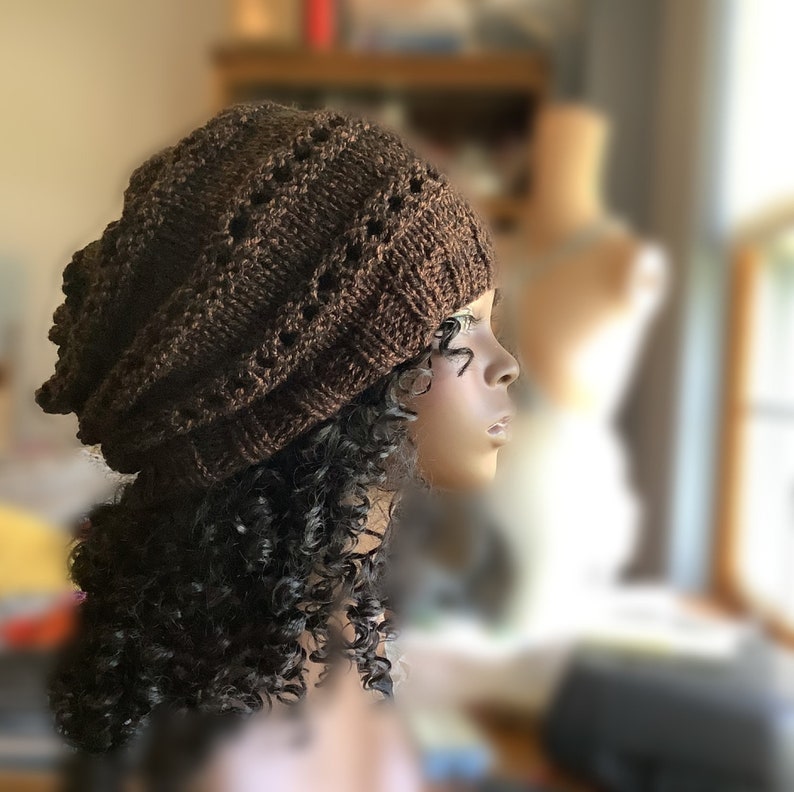 May include: A brown knitted beanie with a lacy pattern. The beanie is slouchy and has a loose fit.