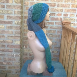Puede incluir: Un gorro de punto azul, verde y gris con una larga bufanda adjunta. El gorro y la bufanda est&aacute;n en un maniqu&iacute;.