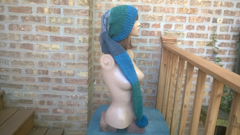 Puede incluir: Un gorro de punto azul, verde y gris con una larga bufanda adjunta. El gorro y la bufanda est&aacute;n en un maniqu&iacute;.