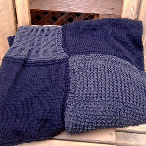 May include: A black and gray knitted blanket with different stitch patterns. The blanket is made of soft yarn and has a cozy feel.