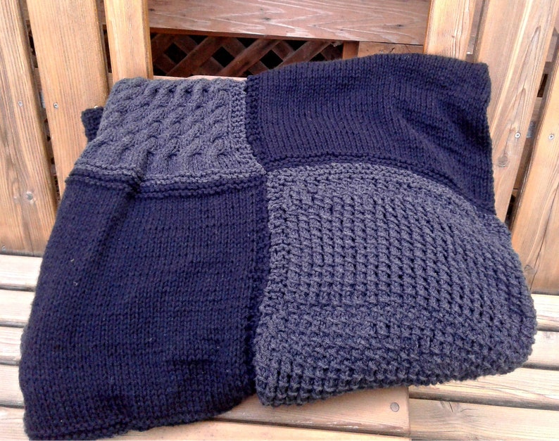 May include: A black and gray knitted blanket with different stitch patterns. The blanket is made of soft yarn and has a cozy feel.
