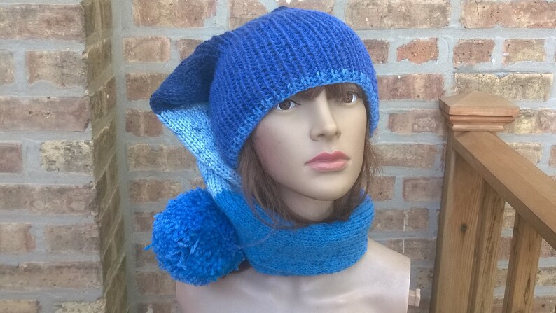 Puede incluir: Un gorro azul de punto con una solapa de oreja larga y puntiaguda y un pomp&oacute;n a juego. El gorro se combina con una bufanda de punto azul.