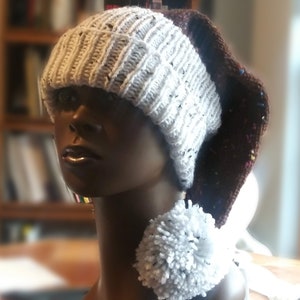 May include: White and brown knitted hat with a white pom-pom. The hat has a slouchy design and is made with a chunky yarn.