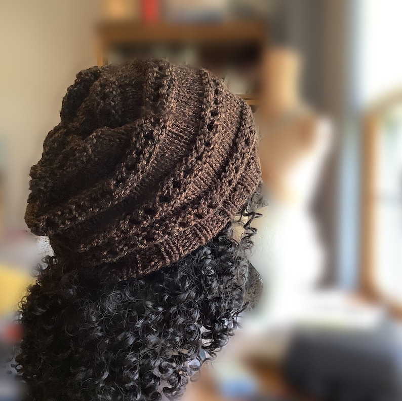 May include: A brown knitted hat with a unique swirl pattern. The hat is made with a soft yarn and has a comfortable fit.