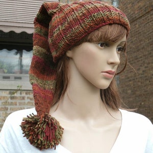 May include: A long, striped knitted hat with a pom-pom on the end. The hat is in shades of brown, green, and red.