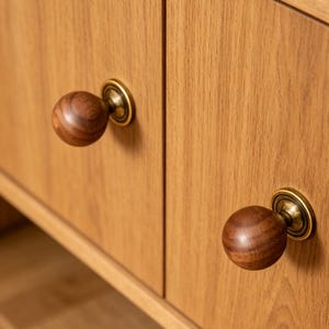 May include: Close-up of two wooden cabinet doors with round, dark brown wooden knobs. The knobs have a brass-coloured base. The cabinet doors are made of light-coloured wood with a visible wood grain.