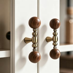 May include: Two cabinet door handles with a modern design. Each handle features a wooden sphere at the top and bottom, connected by a series of brass-colored, rounded links. The handles are mounted on a white cabinet door.