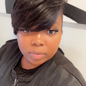 May include: A woman with short black hair wearing a black zip-up shirt.