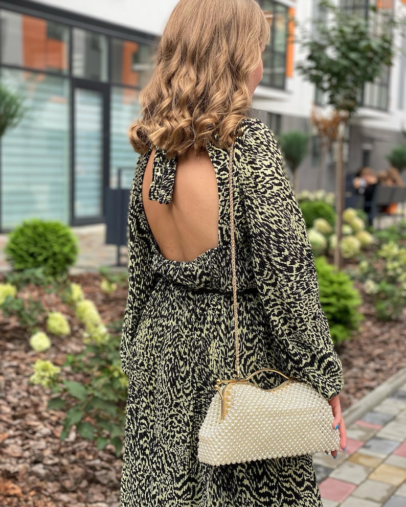 Pode incluir: Uma mulher vestindo um vestido de estampa animal preto e verde com costas baixas e mangas compridas. Ela est&aacute; carregando uma bolsa de m&atilde;o branca de p&eacute;rolas com uma corrente de ouro.