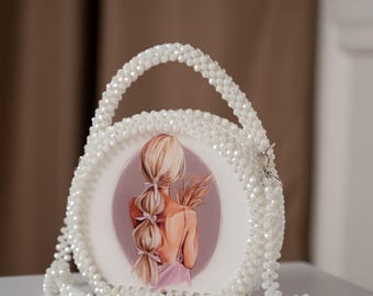 Pode incluir: Uma bolsa branca de contas com uma base redonda branca que apresenta uma ilustração colorida de uma mulher com cabelo longo e loiro. A bolsa tem uma alça branca de contas.