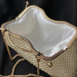Pode incluir: Uma clutch branca de contas de p&eacute;rola com uma al&ccedil;a de corrente dourada e um fecho dourado. A clutch est&aacute; aberta e o interior &eacute; forrado com tecido branco.