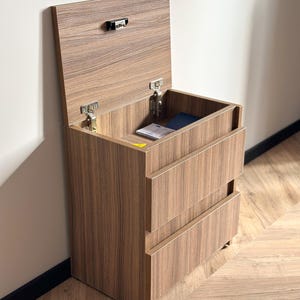 Pu&ograve; includere: Un comodino in legno con un vano superiore sollevabile e due cassetti. Il comodino &egrave; in legno con finitura a venatura marrone. La parte superiore &egrave; aperta, rivelando un piccolo spazio interno. I cassetti sono chiusi.