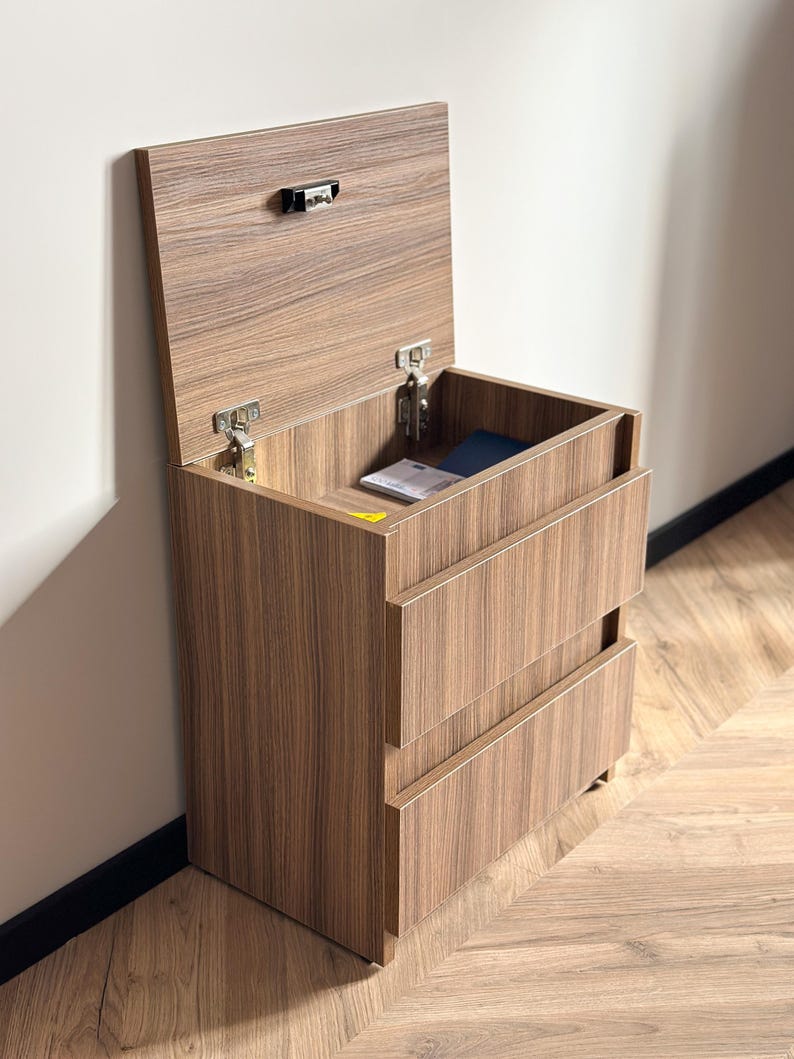 Pu&ograve; includere: Un comodino in legno con un vano superiore sollevabile e due cassetti. Il comodino &egrave; in legno con finitura a venatura marrone. La parte superiore &egrave; aperta, rivelando un piccolo spazio interno. I cassetti sono chiusi.