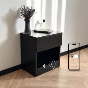 Könnte beinhalten: Ein schwarzer Nachttisch mit Schublade und offenem Regal. Eine Vase mit Trockenblumen, ein Buch und eine Parfümflasche stehen obenauf. Ein Bluetooth-Symbol ist auf dem Nachttisch zu sehen, und ein Smartphone zeigt ein Entsperrsymbol.