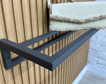 Könnte beinhalten: Ein schwarzes Metallregal mit zwei Ebenen, das an einer Holzwand montiert ist. Eine beige Handtasche mit Fransenbesatz liegt auf der oberen Ablage.