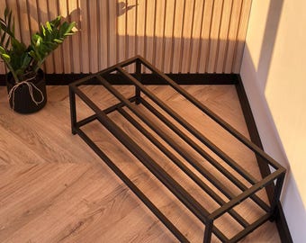 Può includere: Una scarpiera rettangolare costruita con tubi di metallo nero, caratterizzata da un design a telaio a più livelli con barre orizzontali. La struttura è aperta e minimalista, offrendo una base stabile per lo stoccaggio con un aspetto pulito.