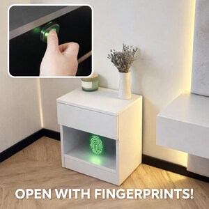 May include: A white bedside table featuring a single drawer with a fingerprint scanner lock. The scanner glows green when activated. A small white vase with dried flowers sits on top. The text "OPEN WITH FINGERPRINTS!" is displayed below.