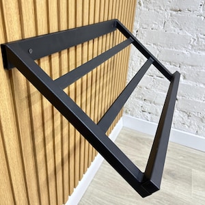 Könnte beinhalten: Schwarzer Schuhregal aus Metall, montiert an einer Wand mit Holzverkleidung. Das Regal hat drei Ebenen zum Aufbewahren von Schuhen.