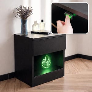 Könnte beinhalten: Ein schwarzer Nachttisch mit einer oberen Schublade und einem offenen unteren Fach, das ein leuchtendes grünes Fingerabdruck-Symbol projiziert. Der Einschub zeigt einen Finger auf einem grünen biometrischen Sensor unter dem Schubladenrahmen.