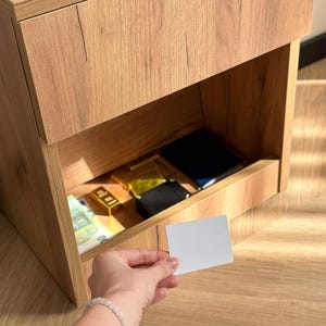 Pode incluir: Uma caneca de cerâmica branca com uma alça preta e o texto "But First, Coffee" em preto, com uma fonte manuscrita. A caneca está sobre uma superfície branca.