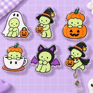 May include: Six acrylic pins featuring light green characters in Halloween costumes: a ghost, a witch with a pumpkin, a character inside a pumpkin, a character in a teacup, a bat, and a witch with a pumpkin attached to a retractable badge reel.