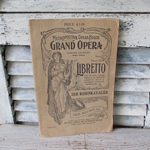 May include: A vintage brown paper libretto for the opera Der Rosenkavalier by Richard Strauss. The cover features a black and white illustration of a woman holding a lyre. The text "Metropolitan Opera House Grand Opera" is printed in bold black letters. The libretto is priced at $1.00.