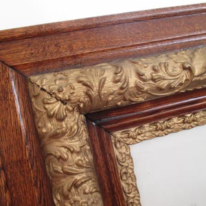 May include: Close-up of a corner of a wooden picture frame. The frame has a dark brown, textured wooden outer edge and a gold-colored, ornate inner edge with floral designs. The frame appears to be antique.